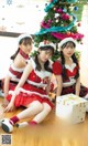 A group of girls in santa outfits sitting next to a Christmas tree.